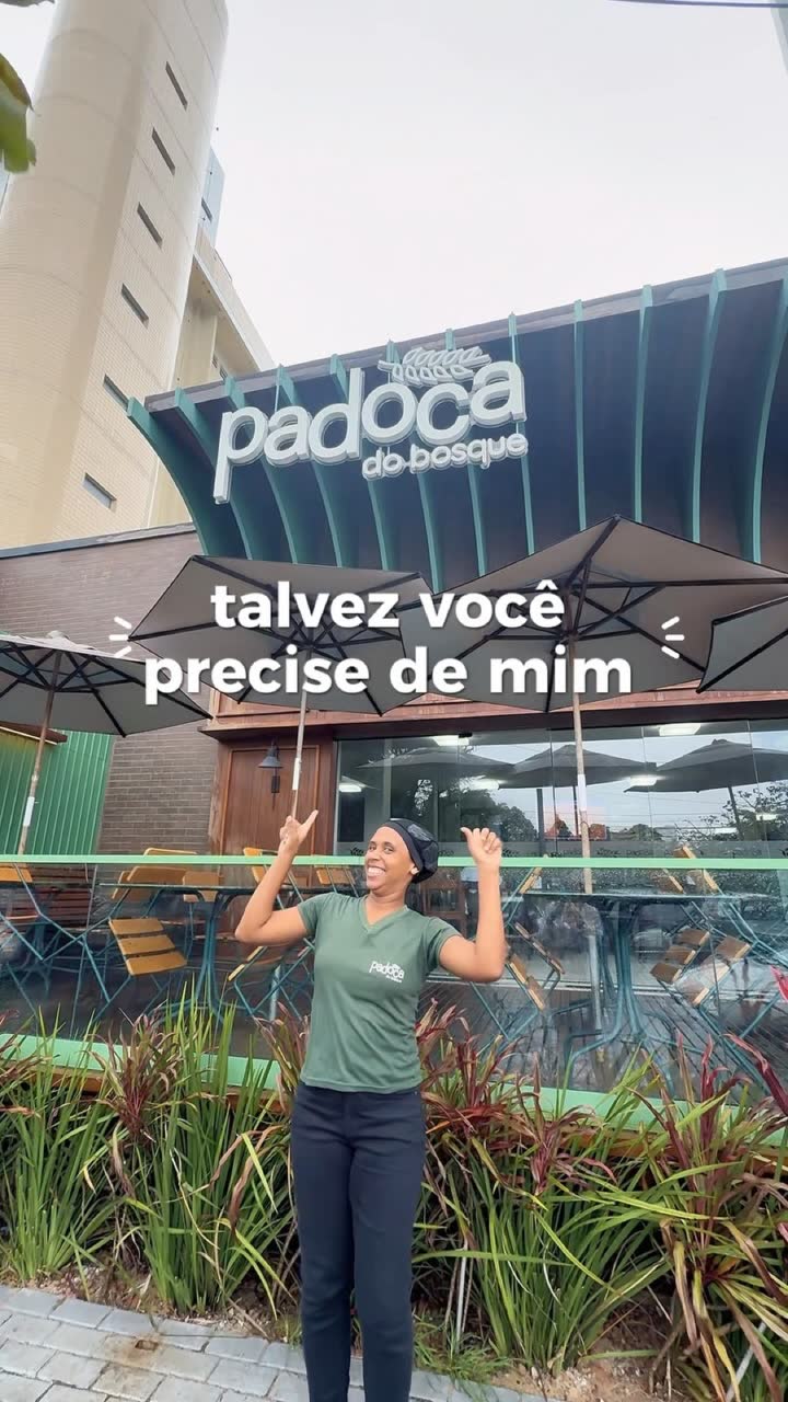 Fachada da Padoca do Bosque: marquise verde canelada com o letreiro padoca do bosque, guarda-sóis e uma funcionária de braços abertos na calçada.