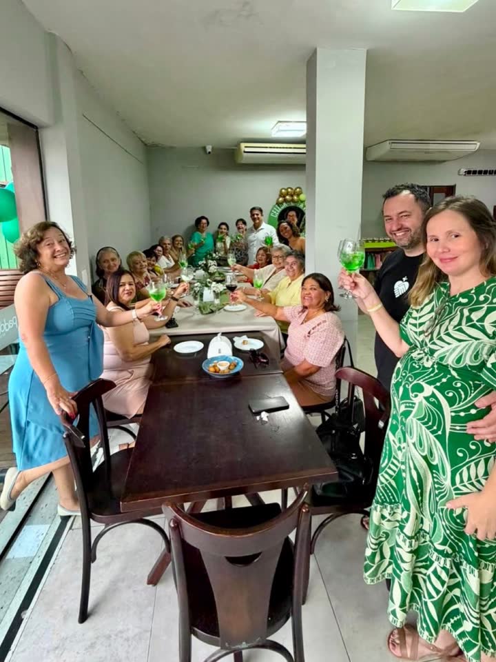 Convidados da festa reunidos em pé e sentados na mesa comprida do salão da Padoca.