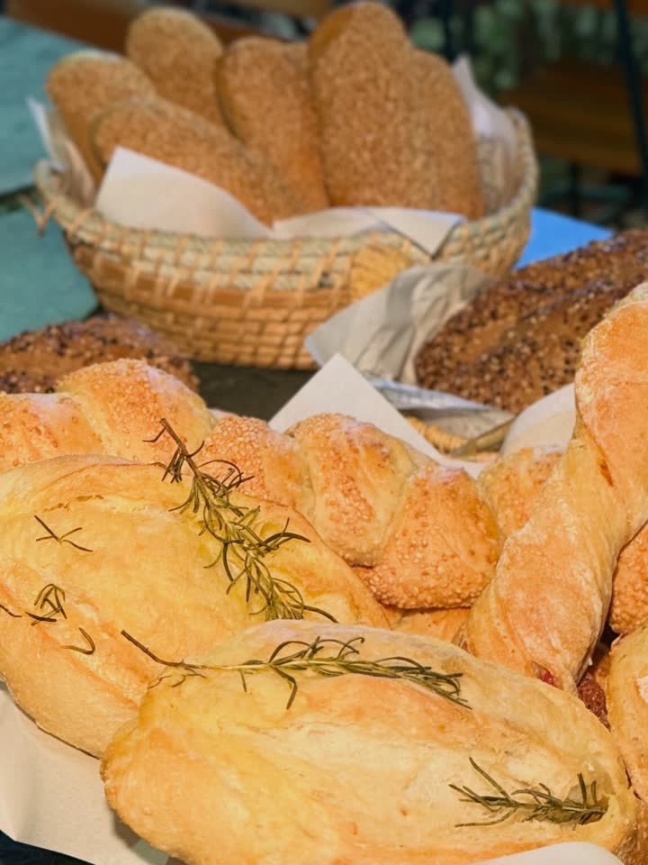 Cesta de vime com pães variados da Padoca e ramos de alecrim sobre a bancada.