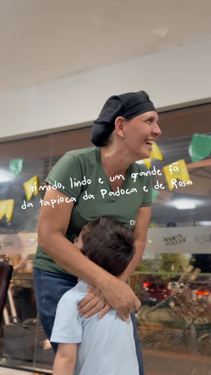 Funcionária da Padoca abraçando um menino no salão, com a legenda escrita à mão pela Padoca chamando ele de grande fã da tapioca da Rosa.