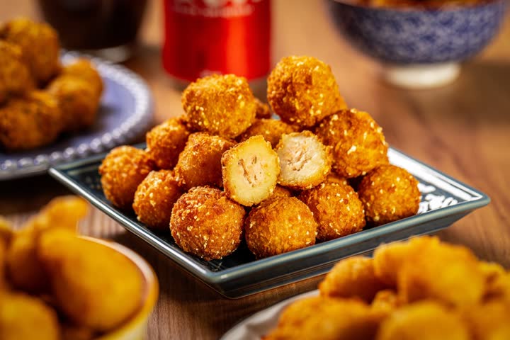 Bandeja de coxinhas e salgados fritos dourados, com um deles partido ao meio mostrando o recheio.